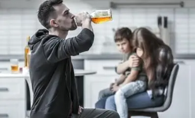 Father drinking alcohol with child and wife in the background.