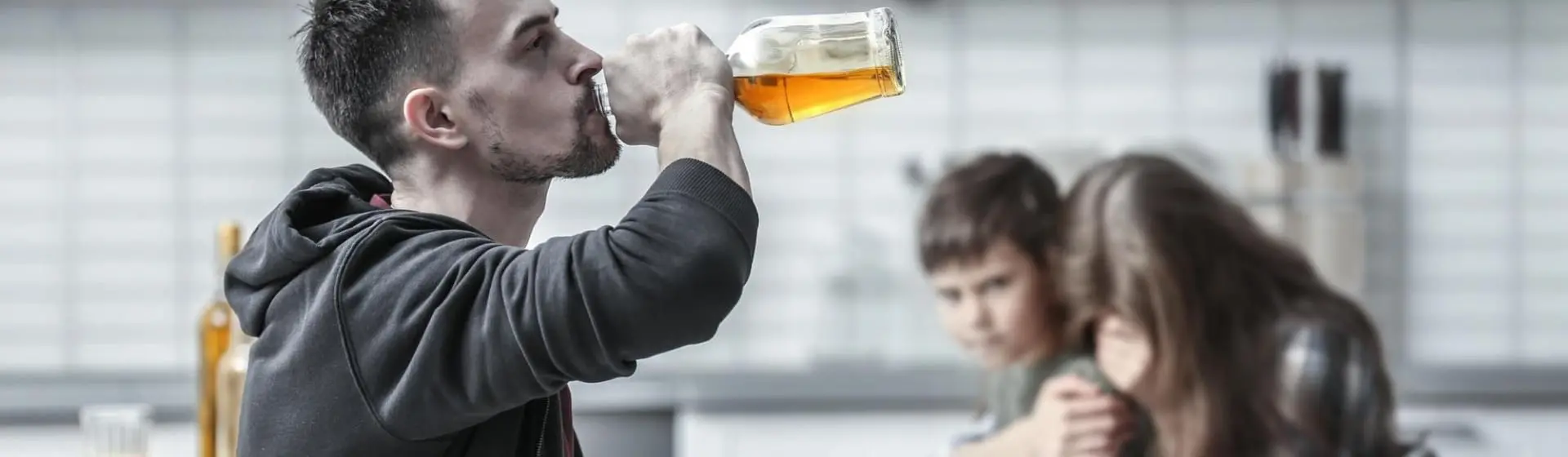 Father drinking alcohol with child and wife in the background.