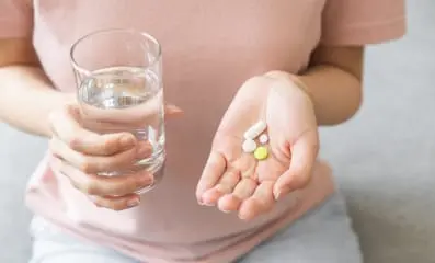 Woman’s hands holding a glass of water and pills. Medications work by reducing cravings and creating unpleasant reactions to alcohol.