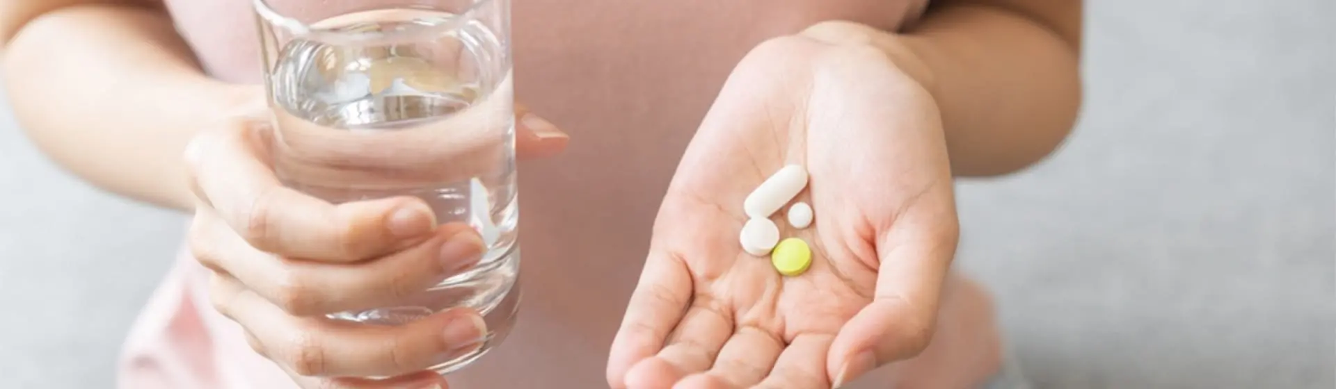 Woman’s hands holding a glass of water and pills. Medications work by reducing cravings and creating unpleasant reactions to alcohol.