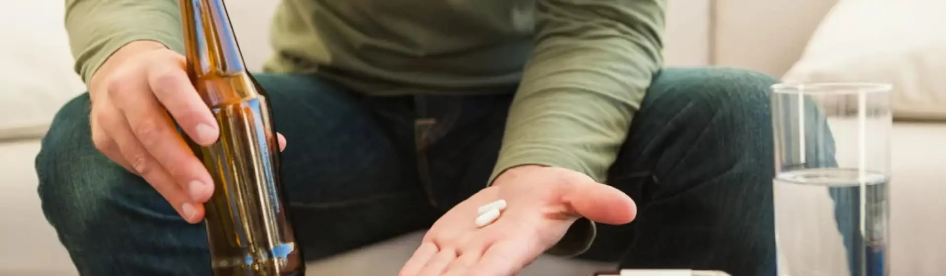 person holding a bottle of liquor in one hand and pills in the other.