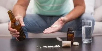 person holding a bottle of liquor in one hand and pills in the other.
