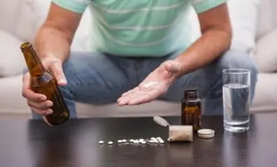 person holding a bottle of liquor in one hand and pills in the other.