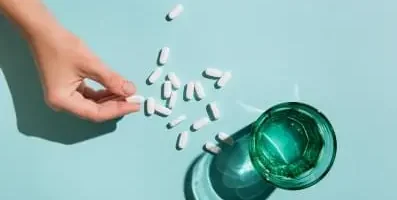 pills scattered on table next to a glass of water