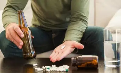 person holding a bottle of liquor in one hand and pills in the other.
