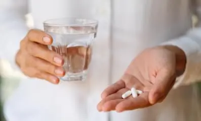 hand holding pills with a glass of water.