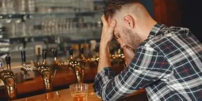 Depressed man at a bar with elbows on table holding his head