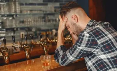 Depressed man at a bar with elbows on table holding his head