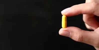 fingers holding yellow pill.