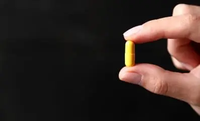 fingers holding yellow pill.
