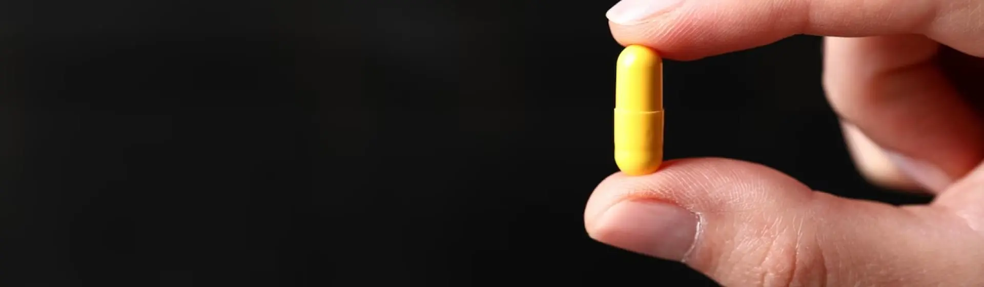 fingers holding yellow pill.