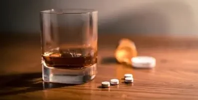 pills on table next to glass of alcohol.