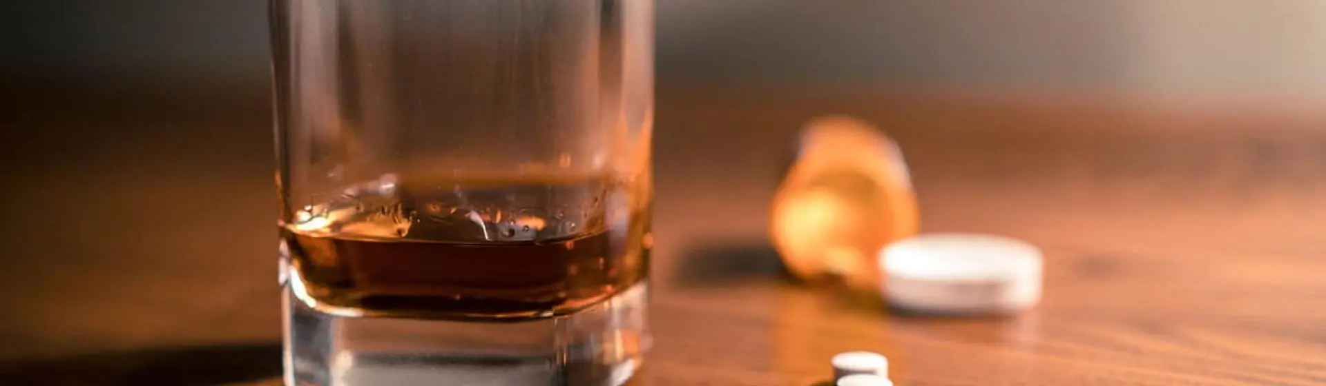 pills on table next to glass of alcohol.