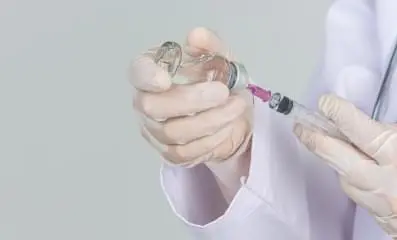Doctor inserting syringe in bottle.