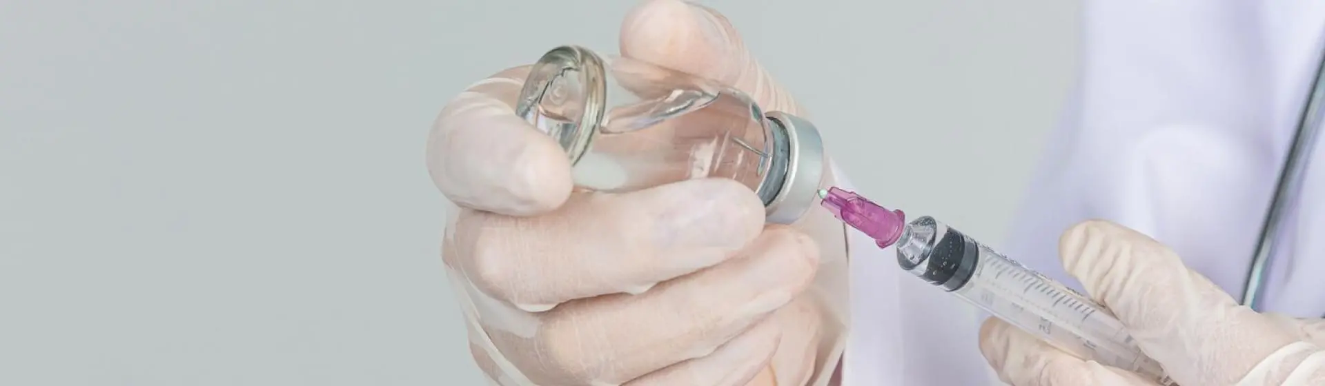 Doctor inserting syringe in bottle.