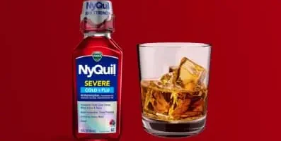 A bottle of Nyquil next to a glass of alcohol.