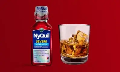 A bottle of Nyquil next to a glass of alcohol.