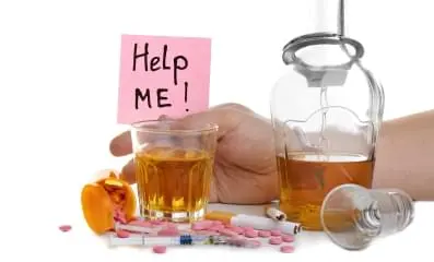 Variety of pills on table with glasses of alcohol and cigarettes. A sign that says help me in the background