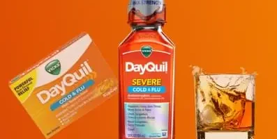 A bottle of Dayquil next to a glass of alcohol.
