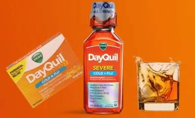 A bottle of Dayquil next to a glass of alcohol.