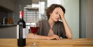 Frustrated woman sitting in front of a bottle and glass of wine.