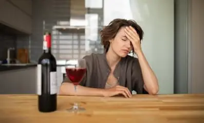 Frustrated woman sitting in front of a bottle and glass of wine.