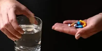 A hand with variety of pills and a glass of water.
