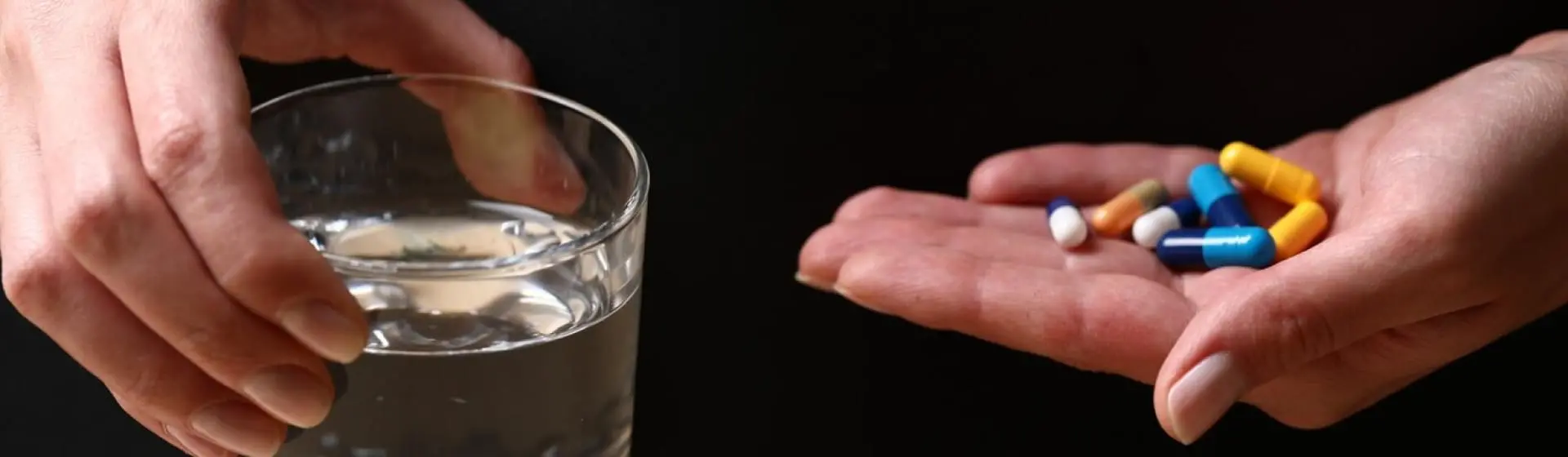 A hand with variety of pills and a glass of water.