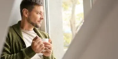 Man holding a mug and looking out a window. Opiate detox involves gradually withdrawing from opioids to manage withdrawal symptoms.