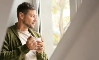 Man holding a mug and looking out a window. Opiate detox involves gradually withdrawing from opioids to manage withdrawal symptoms.