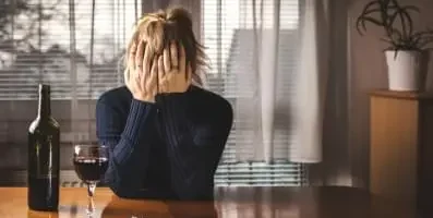Frustrated woman sitting in front of a bottle and glass of wine.