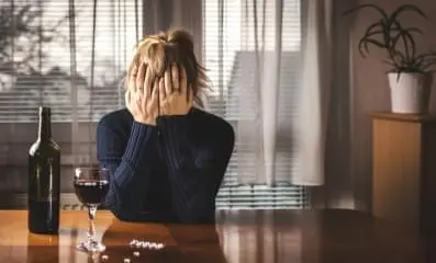 Frustrated woman sitting in front of a bottle and glass of wine.