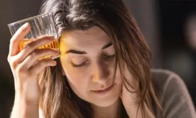 Depressed woman holding a glass of alcohol to her head.