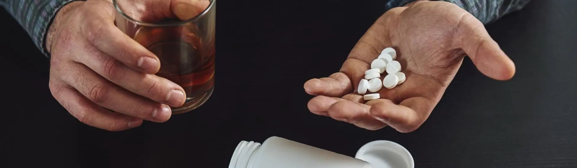 A person holding pills in one hand and glass of alcohol in the other.