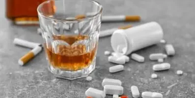 A glass of alcohol, various pills and cigarette on a table.