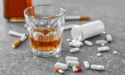 A glass of alcohol, various pills and cigarette on a table.