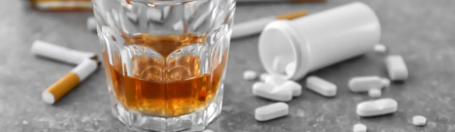 A glass of alcohol, various pills and cigarette on a table.