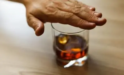 Hand hovering over a glass of alcohol.