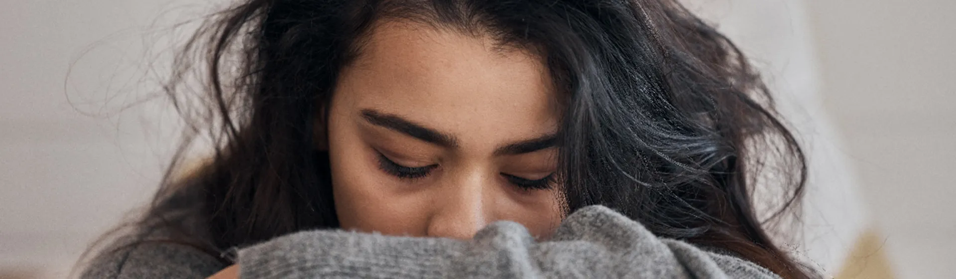 Image of a person with long dark hair, resting their head on their crossed arms and looking down with a sad expression.