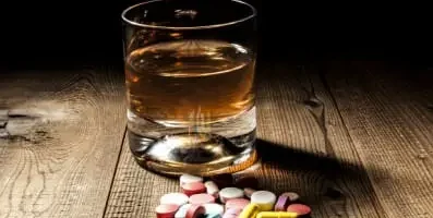 Glass of alcohol next to a pile of pills. Mixing alcohol with drugs intensifies sedative effects, impairing cognitive skills and judgment.