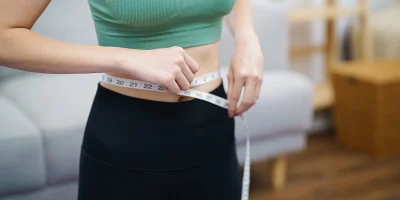 Image of a person in a green crop top measuring their waist with a tape measure.