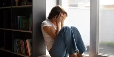 Woman sitting down with hand over her face.