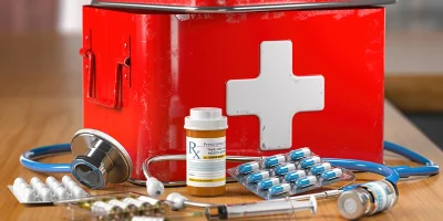 A red medical box with a white cross is surrounded by various medical supplies, including a stethoscope, a prescription bottle, blister packs of pills, and vials with syringes.