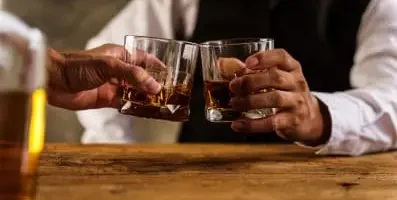Two people holding a glass of liquor.