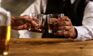 Two people holding a glass of liquor.