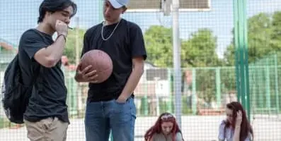 Two teenage boys on an outdoor basketball court, one smokes something.