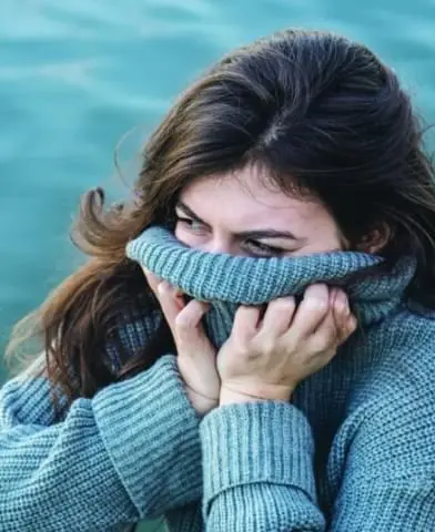 Woman sitting with her turtleneck pulled over her face.