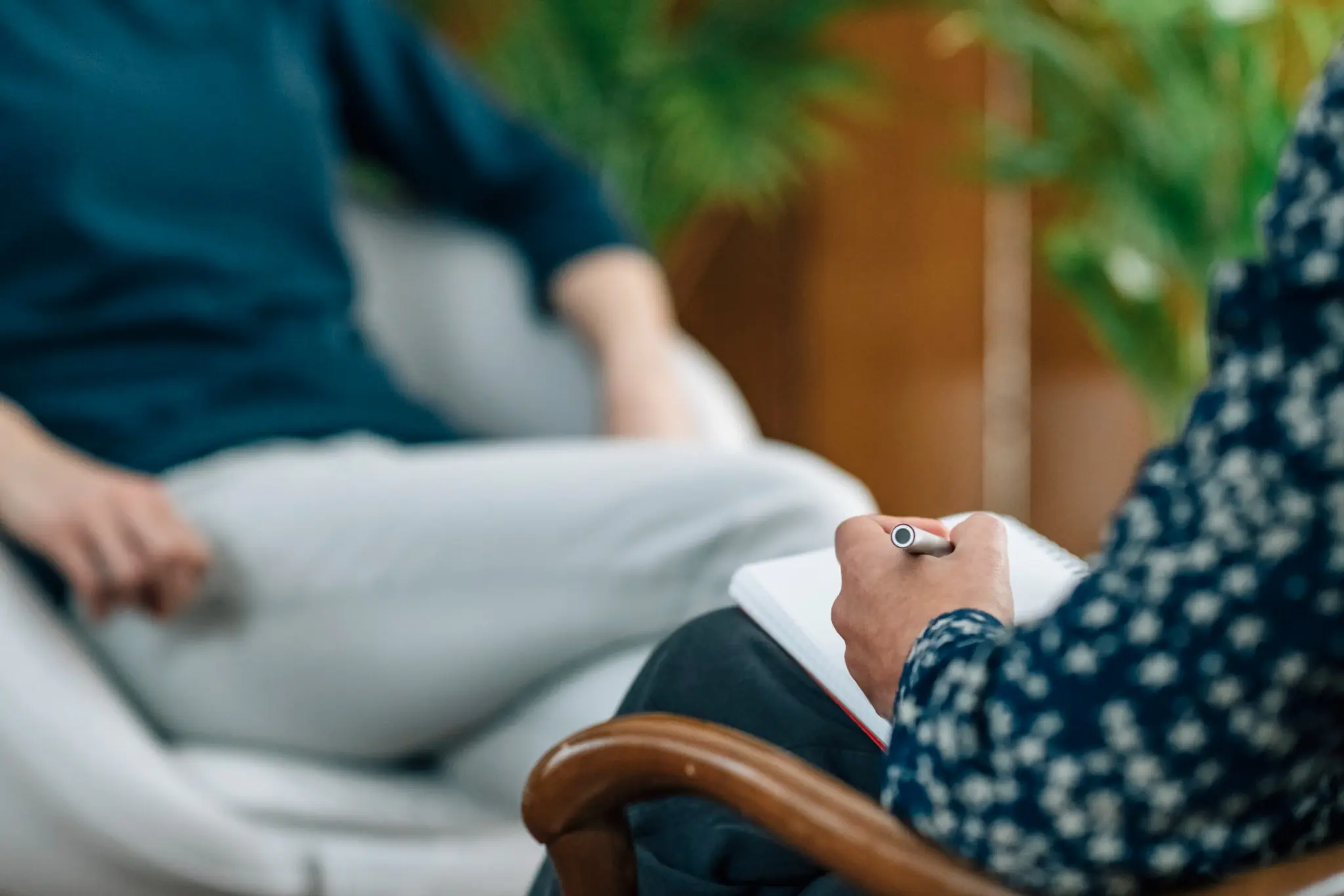 Therapist taking notes during a counseling session with a patient seated in a comfortable, private office setting.