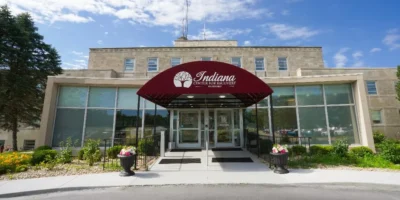 Front entrance of Indiana Center for Recovery with a red awning, glass doors, and landscaped walkway under a blue sky.