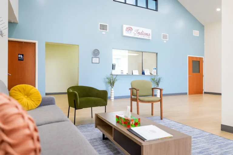 Interior lobby of Indiana Center for Recovery - Terre Haute featuring a blue accent wall, reception window, modern seating, and bright open space.
